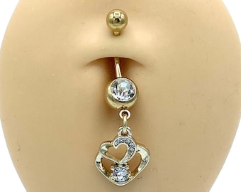 May include: Gold belly button ring with a dangling charm featuring two intertwined hearts with clear rhinestones. The ring has a clear gem on the top and a gold ball on the bottom.