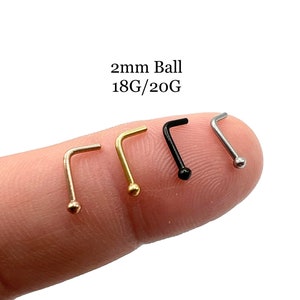 May include: Five nose rings with 2mm balls, shown on a finger. The rings are available in gold, silver, and black.
