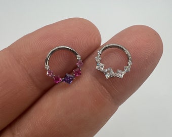 May include: Two silver-colored nose rings. One ring features a gradient of pink and purple square-cut gemstones. The other ring has clear, geometric-shaped stones. Both rings are circular and designed for body piercing.