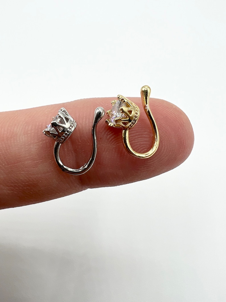 Puede incluir: Dos anillos de nariz con un dise&ntilde;o de corona y una piedra transparente. Un anillo es de oro y el otro de plata.