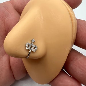 May include: A silver nose ring with a clear crystal crown design.