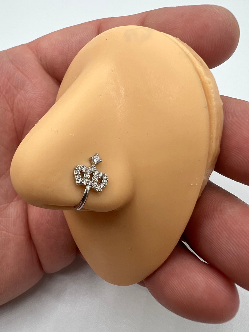 May include: A silver nose ring with a clear crystal crown design.