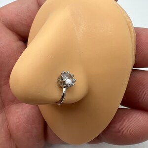 Puede incluir: Un aro de nariz de plata con una piedra de circonita c&uacute;bica transparente engastada en un dise&ntilde;o de corona.