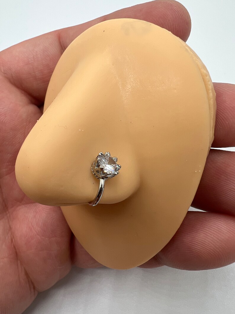 Puede incluir: Un aro de nariz de plata con una piedra de circonita c&uacute;bica transparente engastada en un dise&ntilde;o de corona.