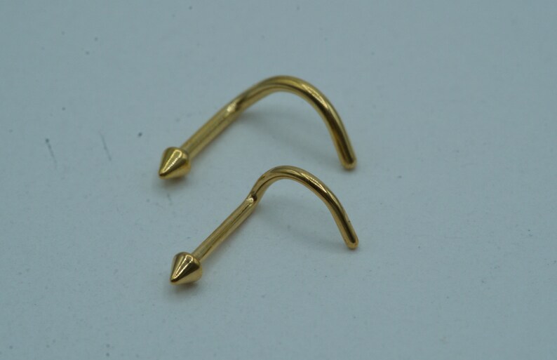 K&ouml;nnte beinhalten: Zwei goldene Nasenringe mit einem spitzen Ende. Die Ringe sind gebogen und haben einen kleinen Durchmesser.