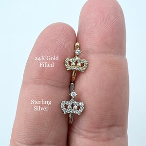 May include: Two nose rings with a crown design. The top ring is 24K gold filled and the bottom ring is sterling silver.