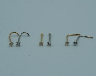Puede incluir: Una colección de joyas para la nariz en tonos dorados y plateados. Los anillos de la nariz presentan pequeñas piedras preciosas transparentes. Los estilos incluyen diseños en forma de L, rectos y enroscados. Las joyas se exhiben sobre un fondo claro.