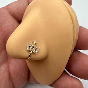 May include: Gold nose ring with a clear crystal crown design.