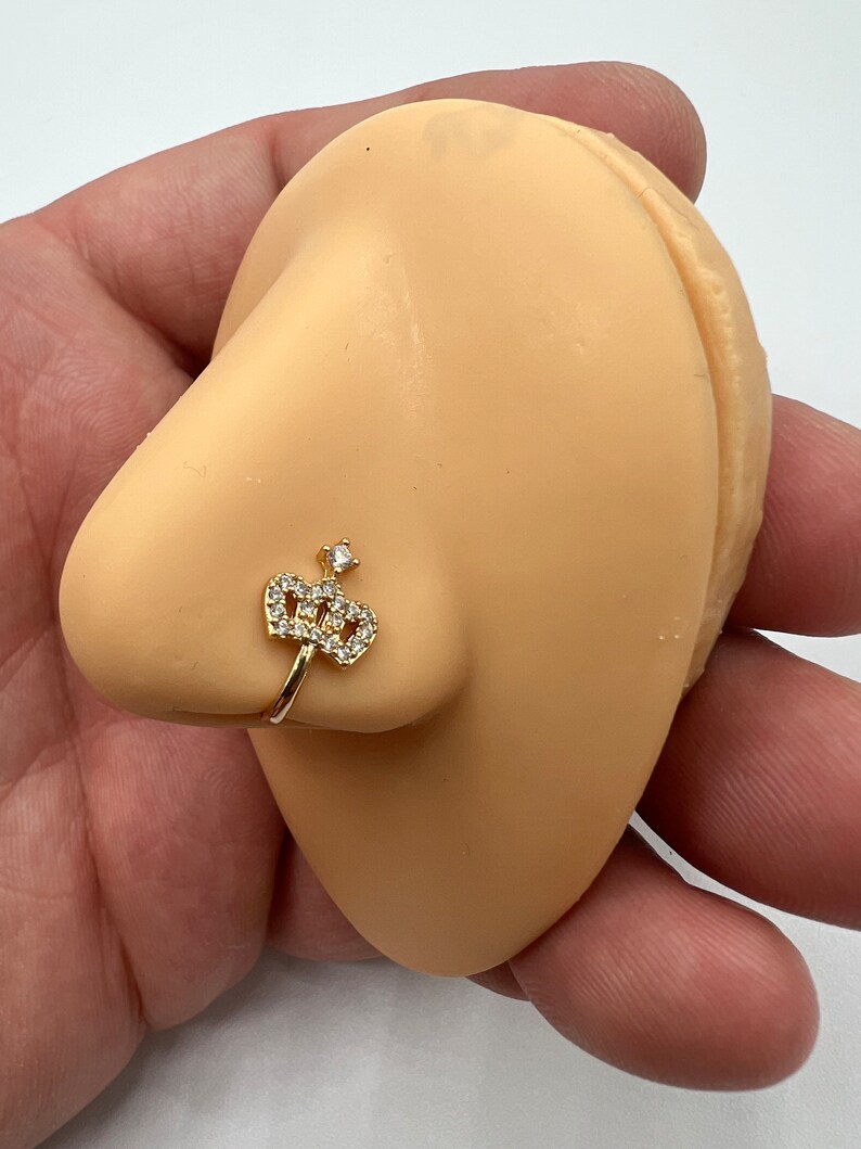 May include: Gold nose ring with a clear crystal crown design.