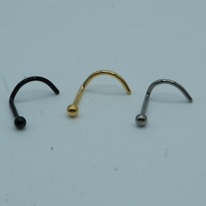 May include: Three nose rings with a curved shape and a small ball at the end. The rings are black, gold, and silver.