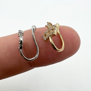 May include: Two nose rings with clear rhinestones. One is silver and the other is gold.