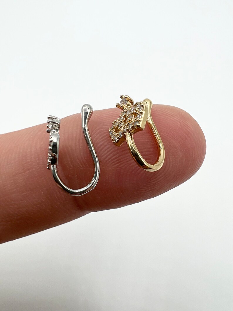 May include: Two nose rings with clear rhinestones. One is silver and the other is gold.