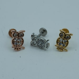 May include: Three owl-shaped body jewelry pieces with clear rhinestones. The pieces are in gold, silver, and rose gold.