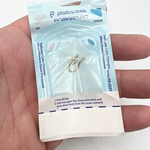 May include: A clear plastic pouch containing a small, silver nose ring. The pouch has a blue and white label that reads "plastcareusa" and "Indicator Color Changes item: PG-2337".