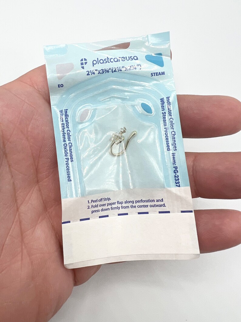 May include: A clear plastic pouch containing a small, silver nose ring. The pouch has a blue and white label that reads "plastcareusa" and "Indicator Color Changes item: PG-2337".