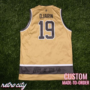 May include: Gold and black custom-made jersey with the name "DJARIN" and the number "19" on the back. The jersey has a white and black trim and a dark gray band at the bottom with stylized text. The words "retro city" are at the bottom left.