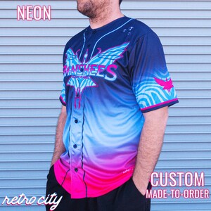 May include: Neon blue, pink and black baseball jersey with a graphic of a bird and the text "Banshees" on the front. The jersey is custom made to order.