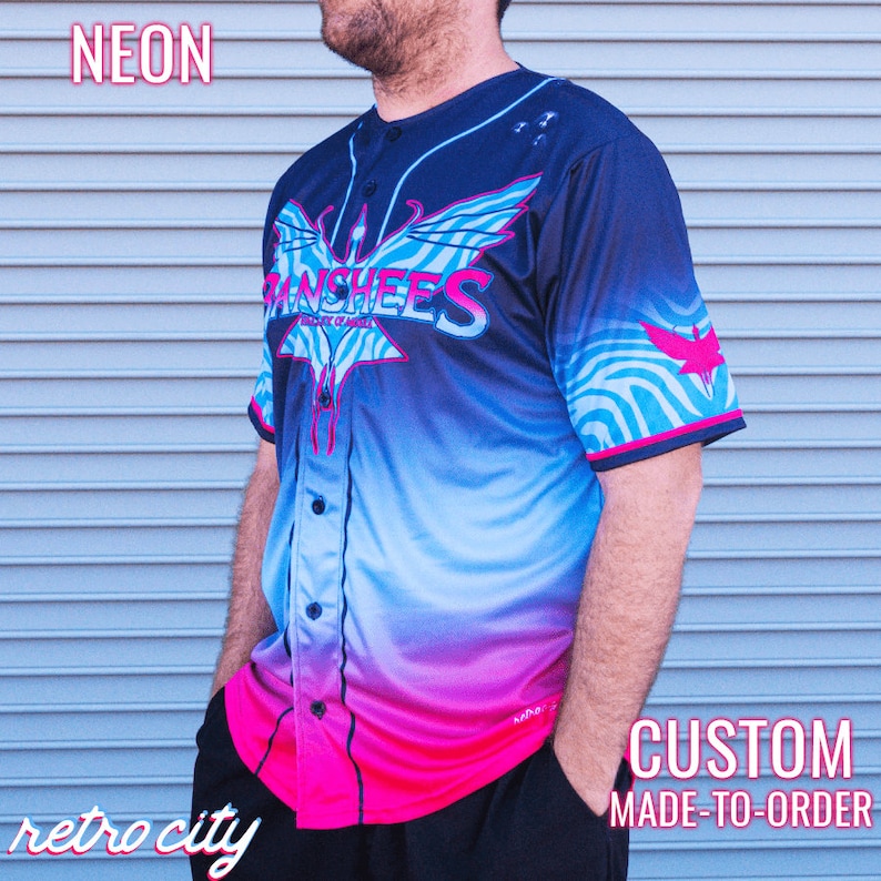 May include: Neon blue, pink and black baseball jersey with a graphic of a bird and the text "Banshees" on the front. The jersey is custom made to order.