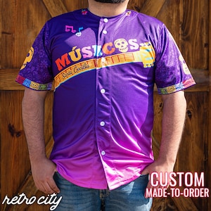May include: A purple baseball jersey with a gradient design, featuring the text "Músicos Santa Cecilia" and musical notes. The jersey has a button-up front and the words "CUSTOM MADE-TO-ORDER" are visible.