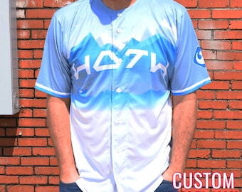 May include: A light blue and white baseball jersey featuring a mountain design and the text "H07W". The jersey has a button-up front and short sleeves with white trim. The words "retro city" are at the bottom left.