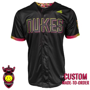 May include: Black baseball jersey with the word "NUKES" in neon yellow and pink lettering. The jersey has a button-up front, short sleeves, and a colorful design on the collar and sleeve cuffs. The text "CUSTOM MADE-TO-ORDER" is also visible.