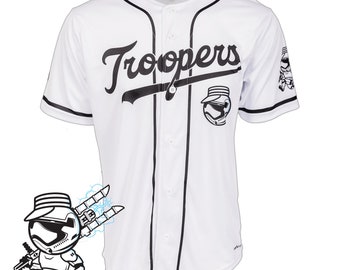 May include: White baseball jersey with black trim, displaying the word "Troopers" in a script font. It features a Stormtrooper helmet graphic and the text "CUSTOM MADE-TO-ORDER". The jersey has a button-up front and short sleeves.