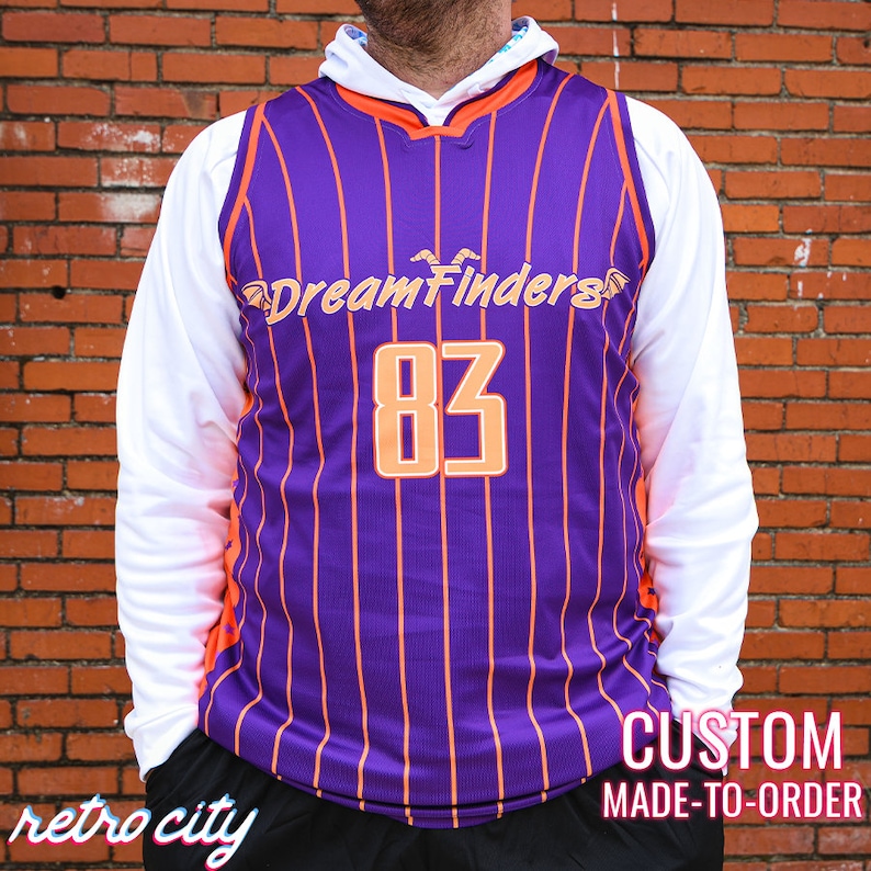 May include: Purple and orange basketball jersey with white stripes and the text "DreamFinders" and the number "83" on the front. The jersey is custom made to order.