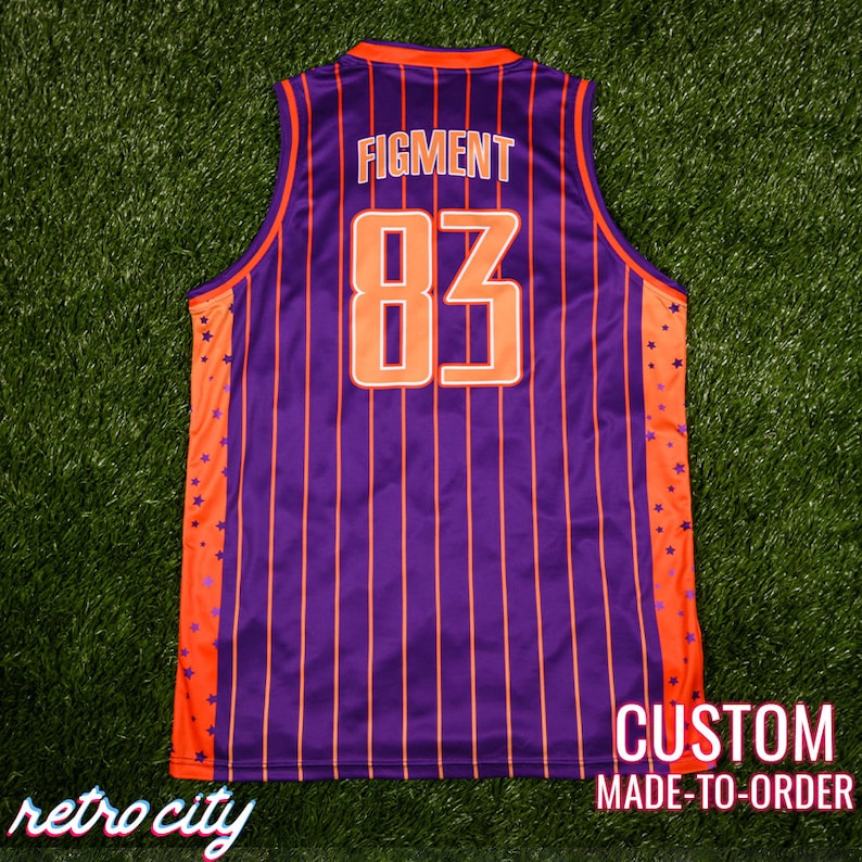 May include: Purple and orange basketball jersey with white vertical stripes and orange stars on the sides. The back of the jersey has the text "FIGMENT" and the number "83" in white outlined in orange. The bottom of the jersey has the text "CUSTOM MADE-TO-ORDER".