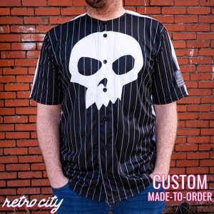 May include: A black and white striped baseball jersey with a white skull and crossbones design. The jersey has a button-up front and short sleeves. The text "CUSTOM MADE-TO-ORDER" is visible at the bottom of the image.