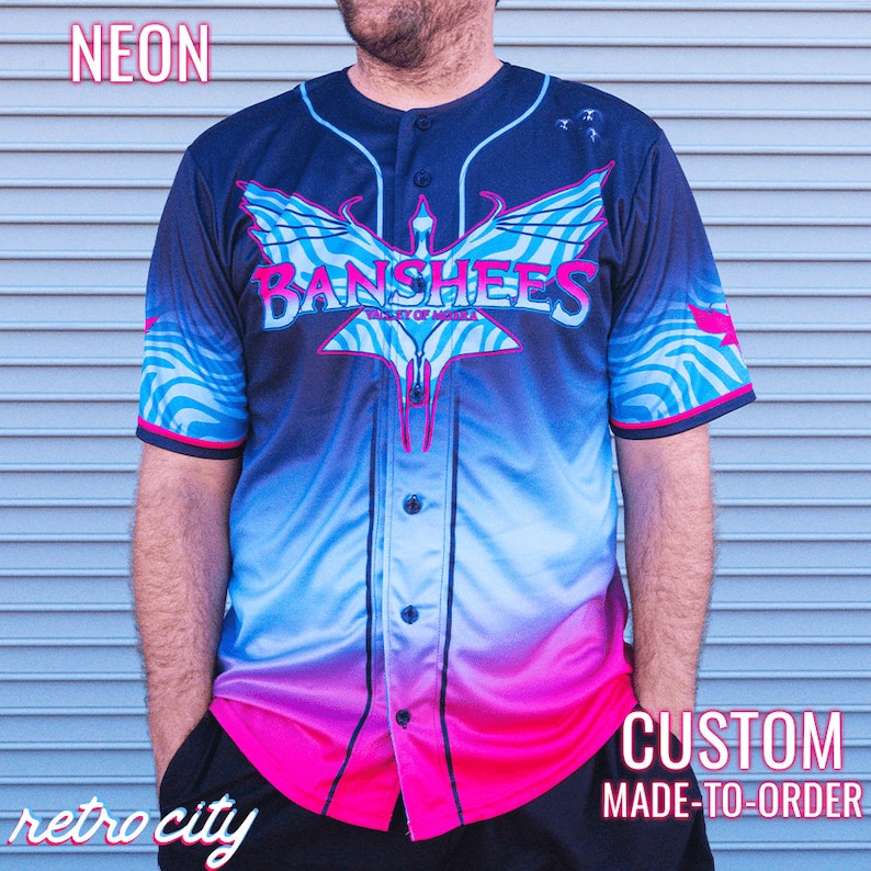 May include: A black baseball jersey with a blue, pink and white gradient design. The jersey features a winged creature with the text "Banshees" and "Valley of Noise" printed on the front.