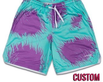 Puede incluir: Shorts deportivos de color turquesa y morado con un estampado personalizado. Los shorts tienen un cordón blanco y un ribete blanco alrededor de los bordes. El texto "retrocity" está impreso en la esquina inferior izquierda de los shorts.