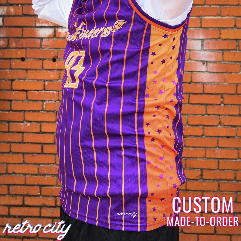 May include: Purple and orange basketball jersey with a striped design and a star pattern on the side. The jersey has the text "Dream Finders" and the number "83" on the front. The text "retro city" is on the bottom of the jersey. The text "CUSTOM MADE-TO-ORDER" is on the bottom right of the image.