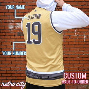 May include: Gold and black custom jersey with the name "DJARIN" and the number "19" on the back. The jersey has a white and grey trim. The words "retro city" and "CUSTOM MADE-TO-ORDER" are also visible.