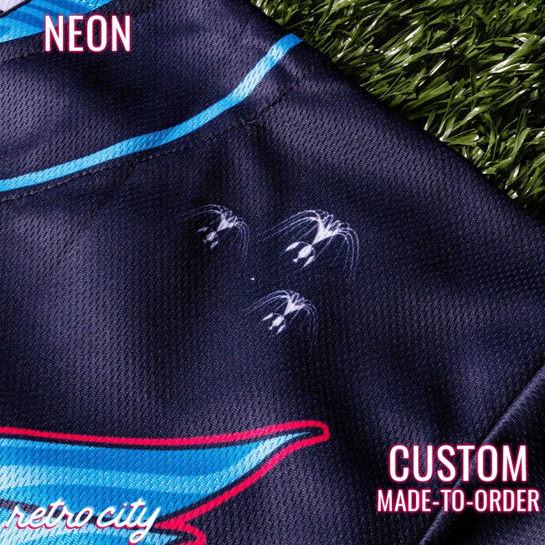 May include: Black and blue jersey with a retro city design and the words "NEON" and "CUSTOM MADE-TO-ORDER". The jersey has a white graphic of three stylised flying creatures.