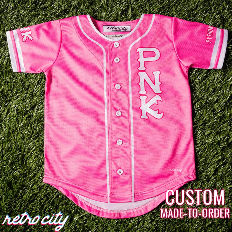 Op de afbeelding: Roze baseballshirt met witte bies en het woord "PINK" in witte letters op de voorkant. Het shirt is op bestelling gemaakt.