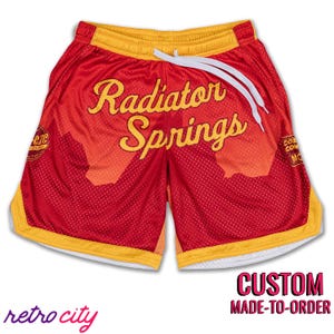 May include: Red and yellow basketball shorts with a white drawstring and "Radiator Springs" printed on the front. The shorts have a mesh design and a white inner lining.