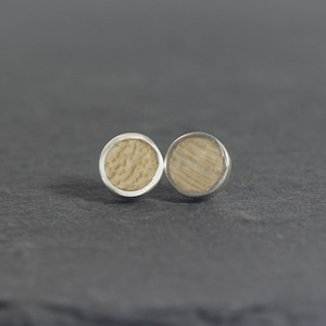May include: A pair of silver stud earrings with a round wooden inlay. The wood is a light brown color with a natural grain pattern.