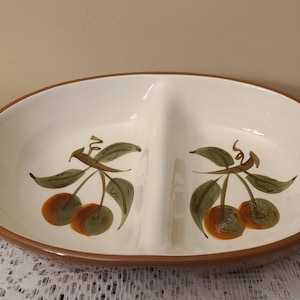 May include: Oval, two-section serving dish with a white interior and a brown rim. The dish is decorated with hand-painted cherries with green leaves and orange-red fruit. A vintage piece for serving snacks or appetizers.
