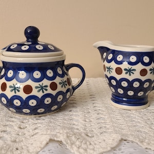 May include: A blue and white ceramic sugar bowl and creamer set with a brown and green floral pattern. The set has a lid and a handle.
