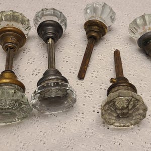 May include: Five antique glass doorknobs with brass and metal hardware. The knobs are clear, faceted, and have a vintage aesthetic. The hardware shows signs of age and wear, adding to their antique charm.