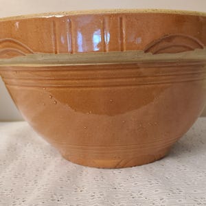 May include: A large, brown ceramic mixing bowl with a wide rim and a rounded body. The bowl features horizontal ridges and decorative carved details near the rim. The bowl is likely vintage and suitable for kitchen use.