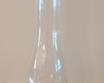 May include: A tall, clear glass lamp chimney with a wide, rounded base that tapers into a slender, cylindrical neck. The glass is transparent and smooth, featuring a flared opening at the top and a circular, open base designed for a lamp.