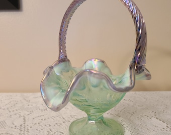 May include: A green iridescent glass bowl with a twisted iridescent handle. The bowl has a ruffled edge and sits on a pedestal.