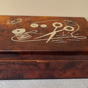 May include: A rectangular, brown sewing box with a glossy finish. The lid features a decorative design of a spool of thread, scissors, buttons, and the words "For my Sewing" in a cursive font. The box is likely made of wood or a similar material.