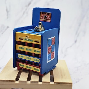 May include: A miniature wooden arcade game with a blue, yellow, and red color scheme. The game has a sign that says "Poker" and a sign that says "Monona". The game has a series of slots with numbers printed on them, including 10,000, 12,000, 15,000, 18,000, 20,000, 25,000, 30,000, 50,000, and 70,000.