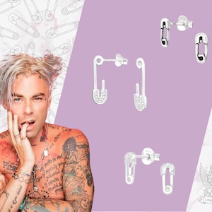 May include: A pair of silver safety pin earrings with clear rhinestones. The earrings are shown on a pink background.