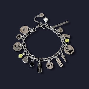 Op de afbeelding: Een zilveren bedelarmband met diverse bedels, waaronder hart-, ronde en rechthoekige vormen. Sommige bedels hebben tekst zoals "GIMME KISS", "FUCKING MAKE ME" en "oke". De armband heeft ook kleine kralen en een sleutelbedel.