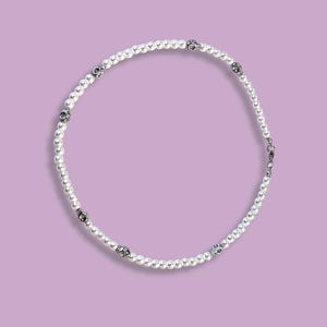 May include: A white pearl necklace with silver skull accents.