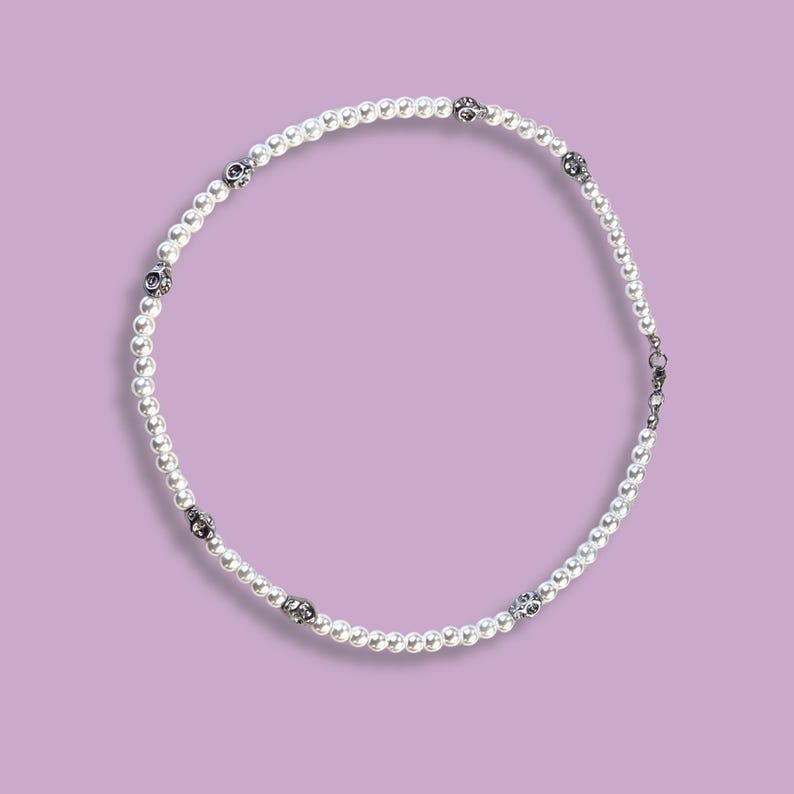 May include: A white pearl necklace with silver skull accents.