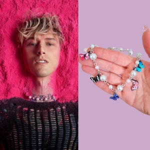 Op de afbeelding: Een zilveren ketting met witte parels en kleurrijke vlinderbedels. De ketting ligt op een hand met een lichtpaarse achtergrond.